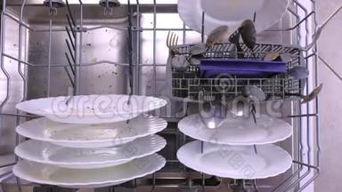 男人`手把一个白色的脏盘子放进洗碗机的篮子里，然后把它推到里面。